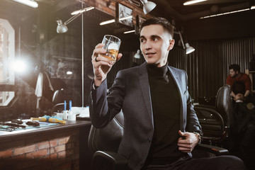 customer smiles/ Successful man in a suit with a glass of whiskey in barbershop