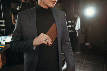 fashion wallet/ A stylish man in a suit puts a leather purse in his jacket pocket