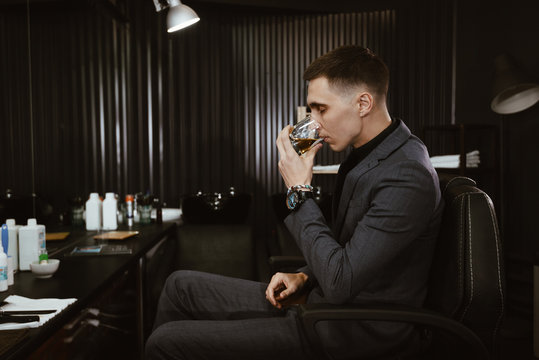 drinks whiskey/ Stylish man with a glass of whiskey in barbershop