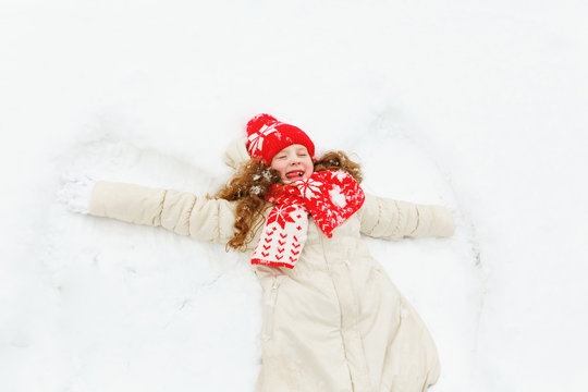 Laughing girl  laying on a snow moving her hand up and down, playing winter outdoors.