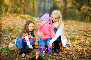 happy family is resting outdoors, mother and children are cooking marshmallows on fire and resting.