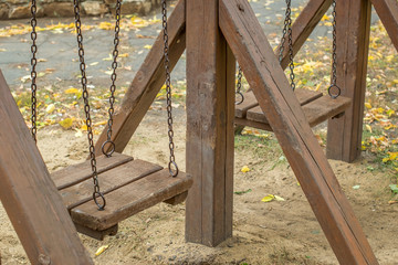 Children's wooden swing on chains in the autumn yard of the park
