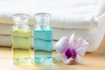 Obraz na płótnie Canvas Mini set of shampoo and shower bath with white bath towel and orchid flower on pine wood table