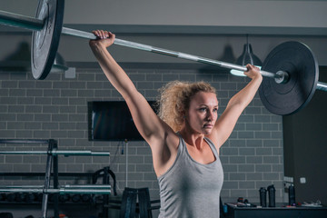 Sport muscular girl raises Barbell on CrossFit in the gym