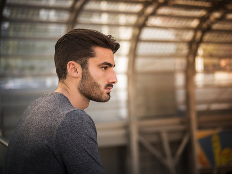 Handsome young man profile shot, indoor, inside big modern building, maybe a brand new train station, looking far