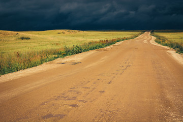 Fototapeta na wymiar Dirt road to the horizon line under dramatic dark storm clouds.