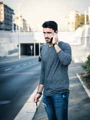 Handsome man making a phone call, talking on cell phone, standing outdoor during daytime in business district