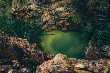The underground green lake is surrounded by vegetation and rocks. © Daniil