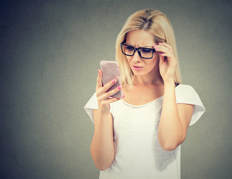 Annoyed upset woman in glasses looking at her cell phone with frustration