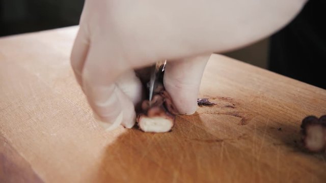 Chef hand holding octopus and tentacles with knife. Seafood restaurant close up slice cut