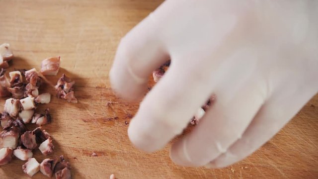 Chef hand holding octopus and tentacles with knife. Seafood restaurant close up slice cut