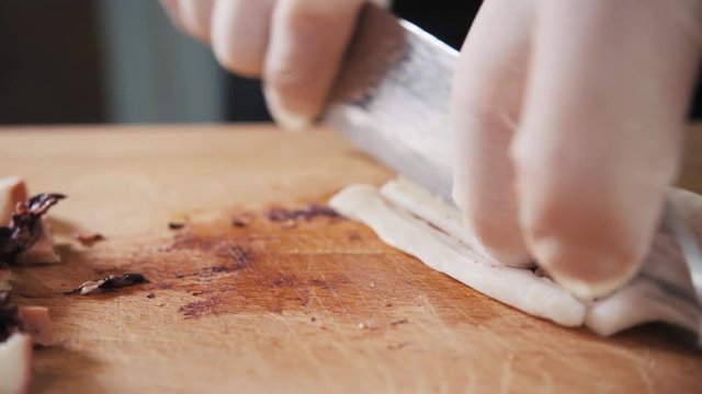 Chef hand holding octopus and tentacles with knife. Seafood restaurant close up slice cut