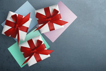 Three gift boxes with red satin ribbon and different color papers, on blue background, top view