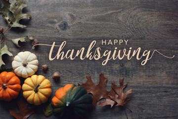 Happy Thanksgiving greeting text with colorful pumpkins, squash and leaves over dark wooden...