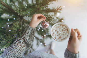 A girl drinks cacao with marshmallo and decorates a Christmas tree.