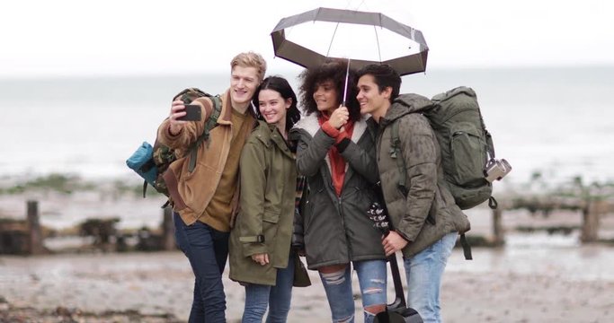 Group of young adult friends taking a selfie on a beach in winter