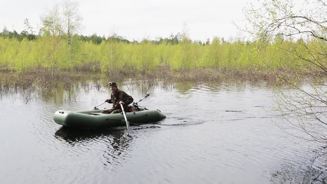 A man swims along the forest river in flood in a rubber boat
