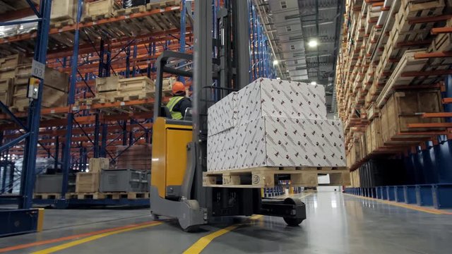 warehouse worker driver in uniform loading cardboard boxes by forklift stacker loader furnirure storage boards