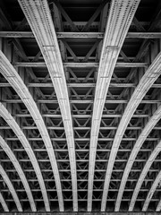 Black and white image of steel arches under a bridge