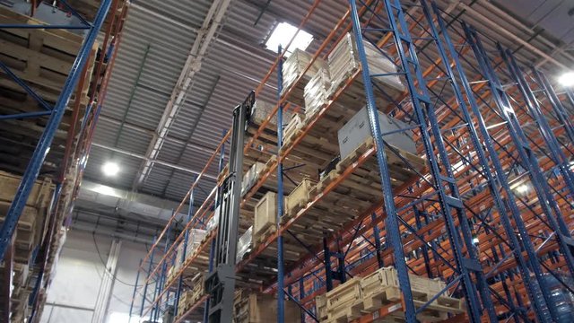 warehouse worker driver in uniform loading cardboard boxes by forklift stacker loader furnirure storage boards