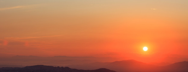 Beautiful sunset on sky over mountains background. The sun is on the right side.