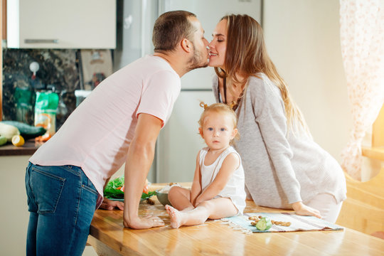 Couple Kissing While Their Baby Sitting Under Them On Table