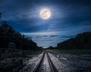 Blue sky and full moon above silhouettes of trees and railway.