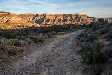 Rough dirt road below desert mesas at sunset