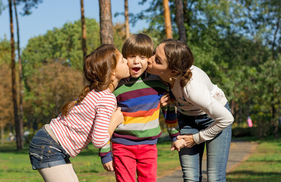 Mom and sister kiss the boy from both sides.