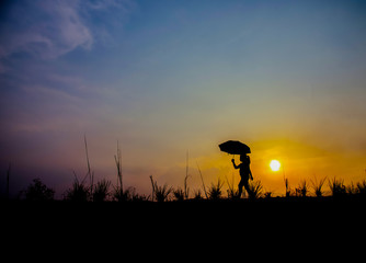 The girl is walking on an umbrella on a meadow at sunset.