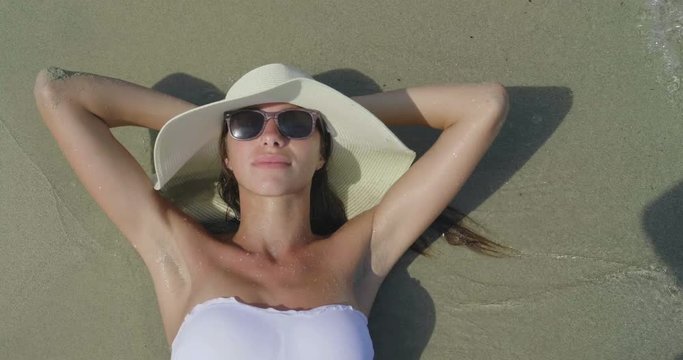 Portrait of a beautiful young girl, woman sunbathing on the sea, in a swimsuit, white hat, sea and sand background. Concept sea rest, clean air, freedom, sun, travel, vacations, sunglasses, enjoy.