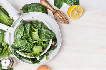 Colander with spinach and vegetarian ingredients on white wooden background, top view, place for...