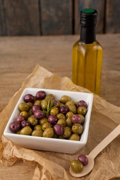 Olives with rosemary served in bowl by oil bottle on table