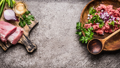 Meat on cutting board with  minced meat, spoon and ingredients on gray rustic background, top view, place for text, frame. Cooking,recipes and eating concept