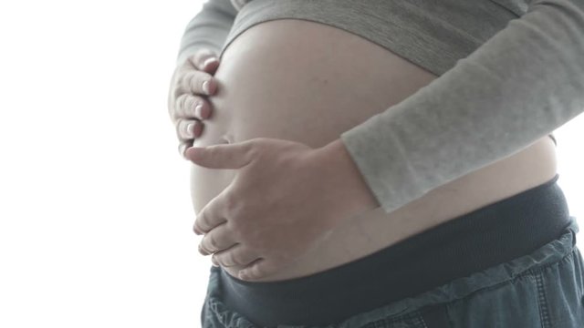 Pregnant woman touching and rubbing her belly, mother stroking and stimulating abdomen, adult caucasian female in fifth month (twenty first week - second trimester) of pregnancy, ungraded flat footage