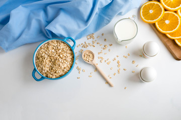 Oat flakes plate with milk, orange, eggs on a wooden white table. Top view of healthy oat flakes breakfast. Copy space. proteins and carbohydrates balanced Breakfast diet