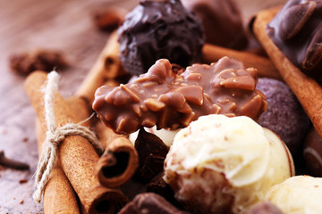 A selection of assorted chocolate truffle pralines on a wooden table with dark chocolate, cinnamon and anise.