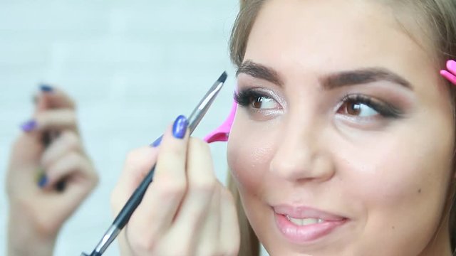 Professional make-up artist applying mascara on eyelashes of model in white room.