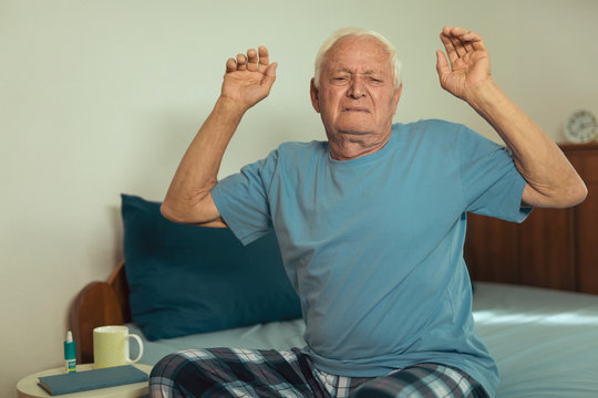 Senior Man Waking Up And Stretching In Bedroom