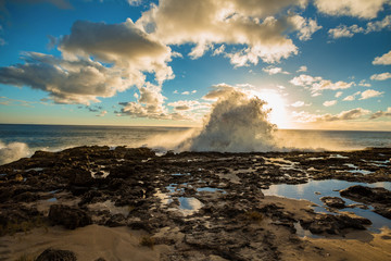 Ocean water waves crashing against rocks on shore during sunset