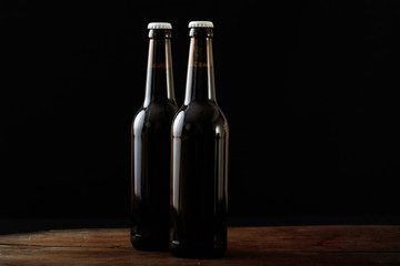 Closeup of two beer bottles isolated on a wooden table, black background
