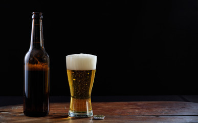 A bottle and a glass of beer on a wooden table, dark background