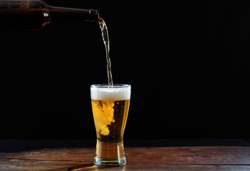 Pouring beer in a glass on a wooden table, dark background