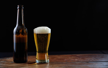 A bottle and a glass of beer on a wooden table, dark background