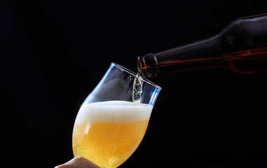 Pouring beer in a glass closeup, black background