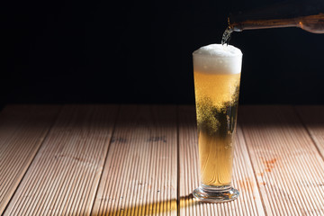 Pouring beer in a glass on a wooden table, dark background