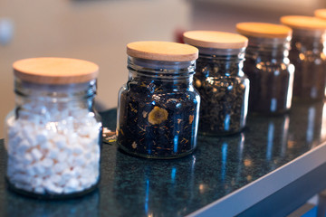 Different types of tea in glass jars on a blurred background.