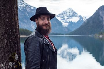 Stylish tattoed Hipster Man enjoys scenic mountain lake in Austria