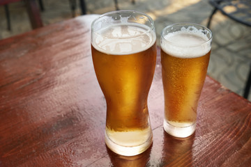 Glasses of fresh beer on wooden table outdoors