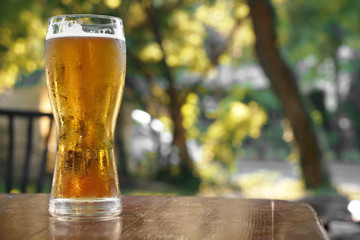 Glass of fresh beer on wooden table outdoors